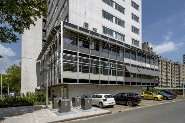 Moderne witte kantoorgebouw aan de Van Leijenberghlaan met parkeerplaatsen en ondergrondse afvalcontainers op de voorgrond.